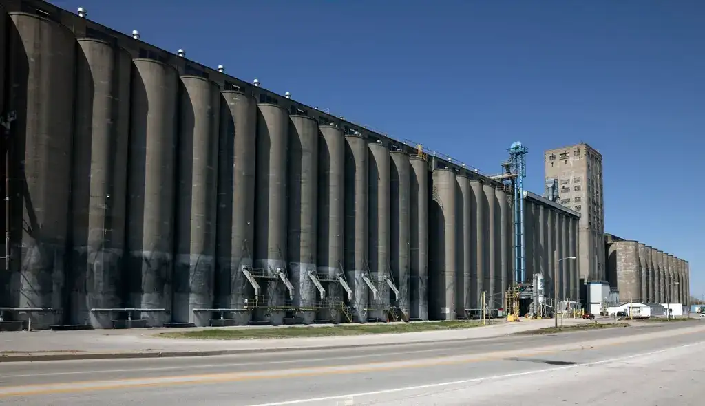 A block-long concrete grain elevator beside a four-lane road under a clear sky