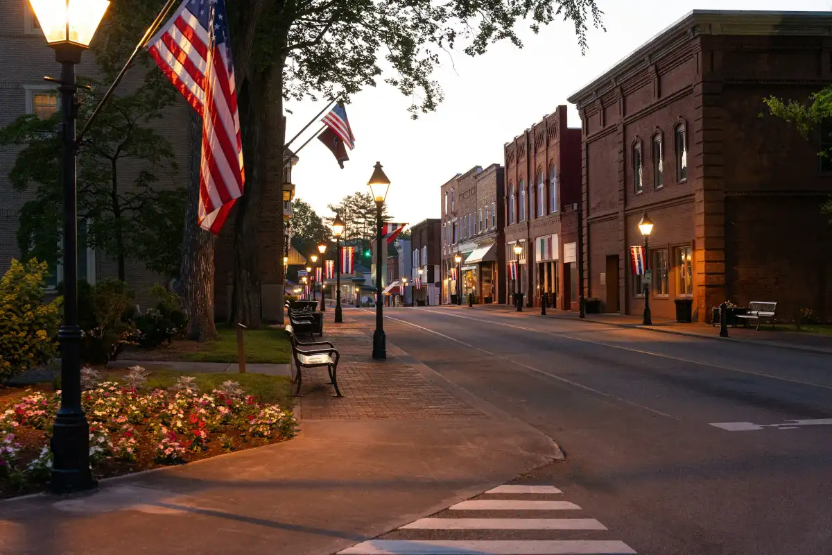 A small-town main street at dusk with flags, street lamps and brick storefronts