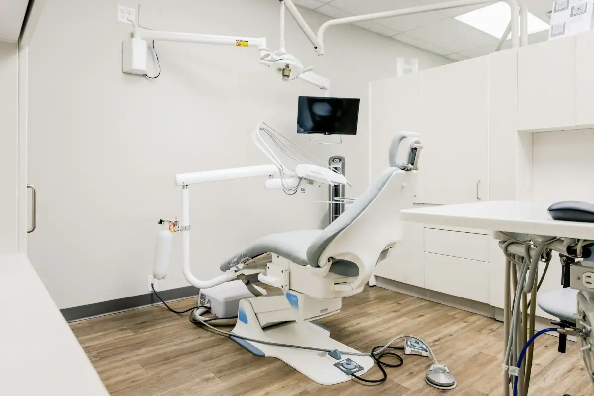 An empty dental treatment room with a gray chair, an overhead light and a wall monitor (stock photo)