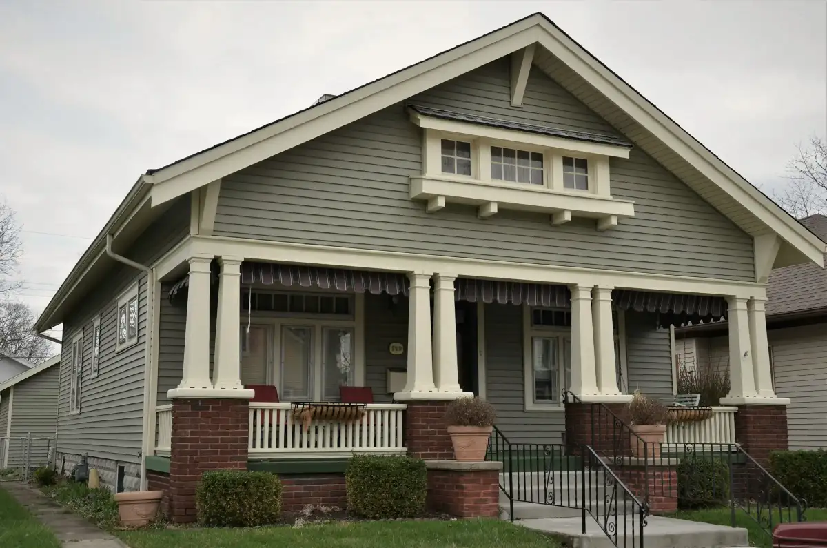 A sage-green Craftsman bungalow with a deep front porch and white columns