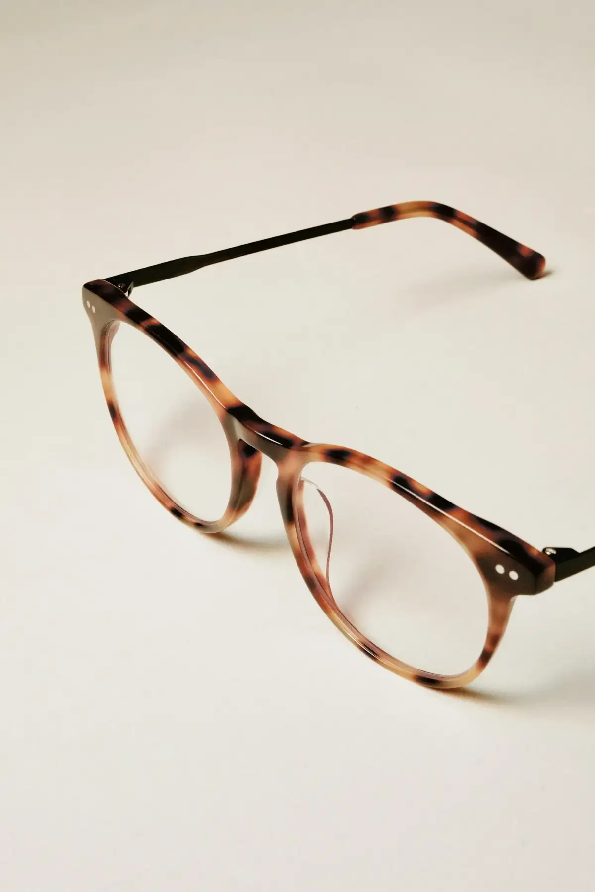 Round tortoiseshell glasses lying open on a pale table (stock photo)